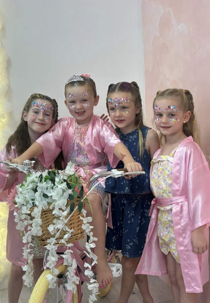 Group of children in pink robes beside a decorative flower bicycle