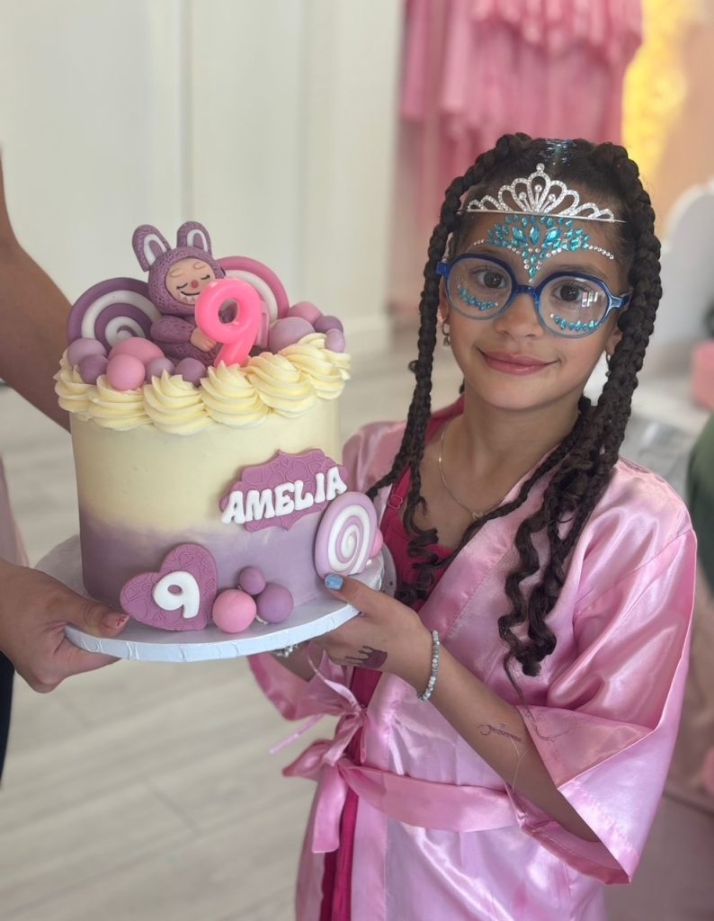 Child in a pink robe holding a personalised birthday cake at a pamper party